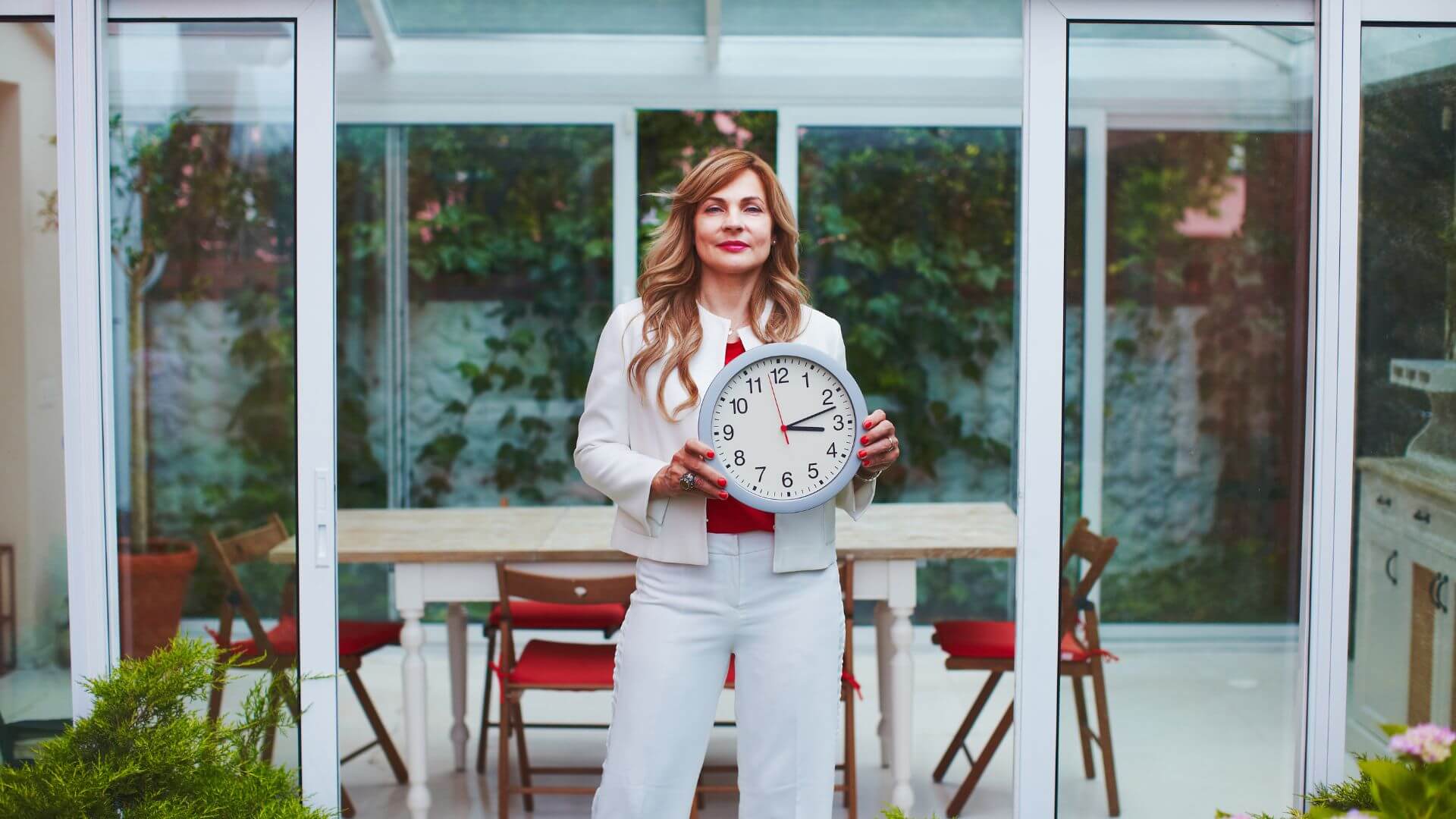 a woman holding a clock in front of a glass door