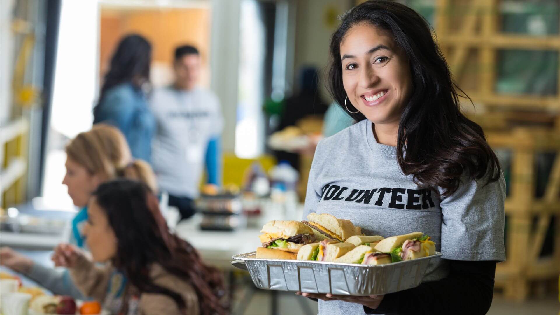 a woman holding a tray of sandwiches in front of a group of people