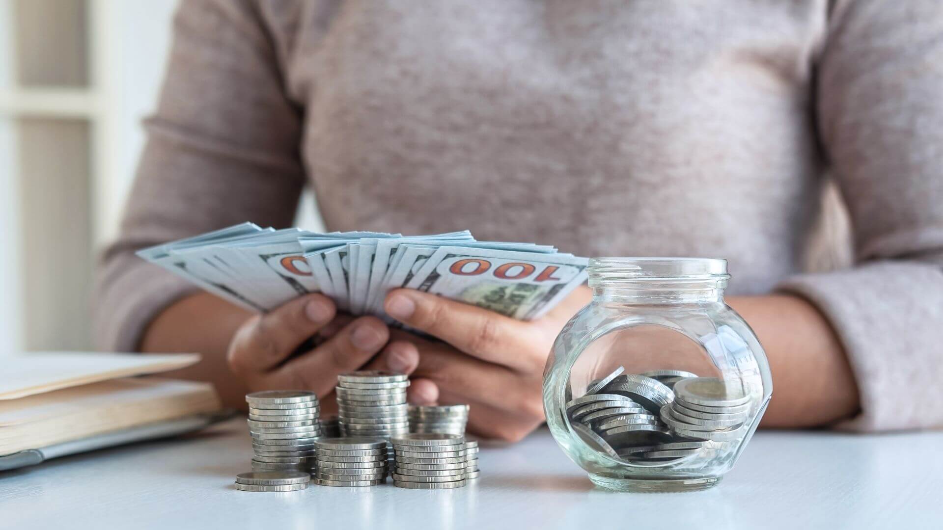 a woman is holding money in front of a glass jar