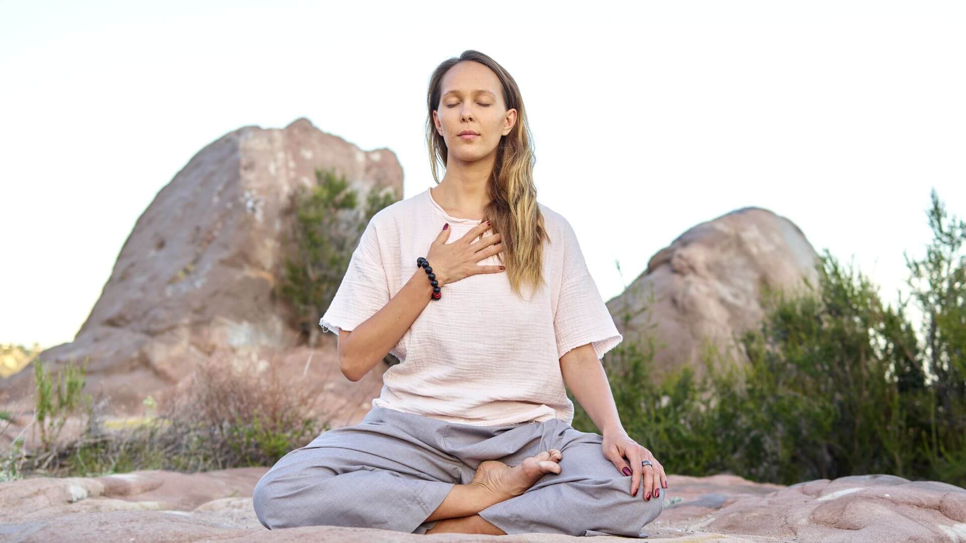 a woman is meditating on a rock in the desert