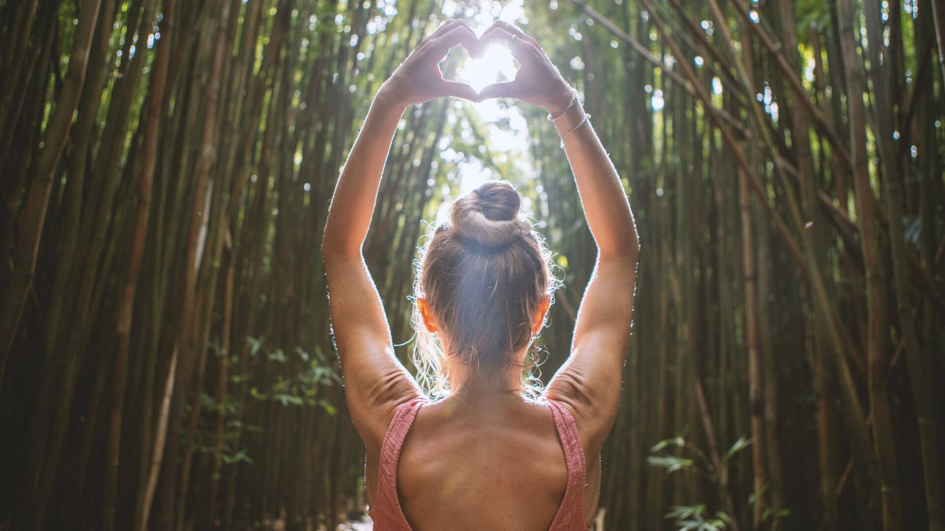 a woman is standing in a bamboo forest making a heart shape with her hands 2