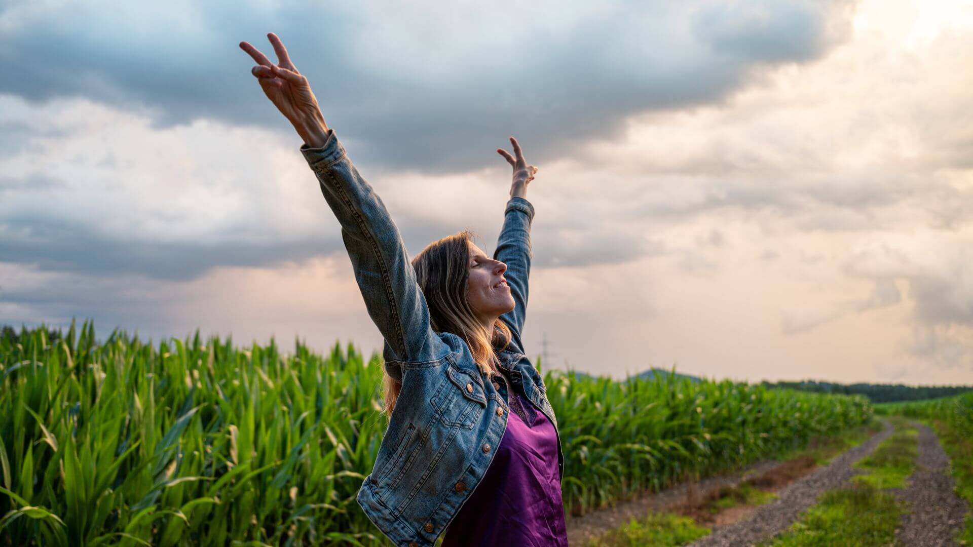 a woman is standing in a corn field with her arms raised