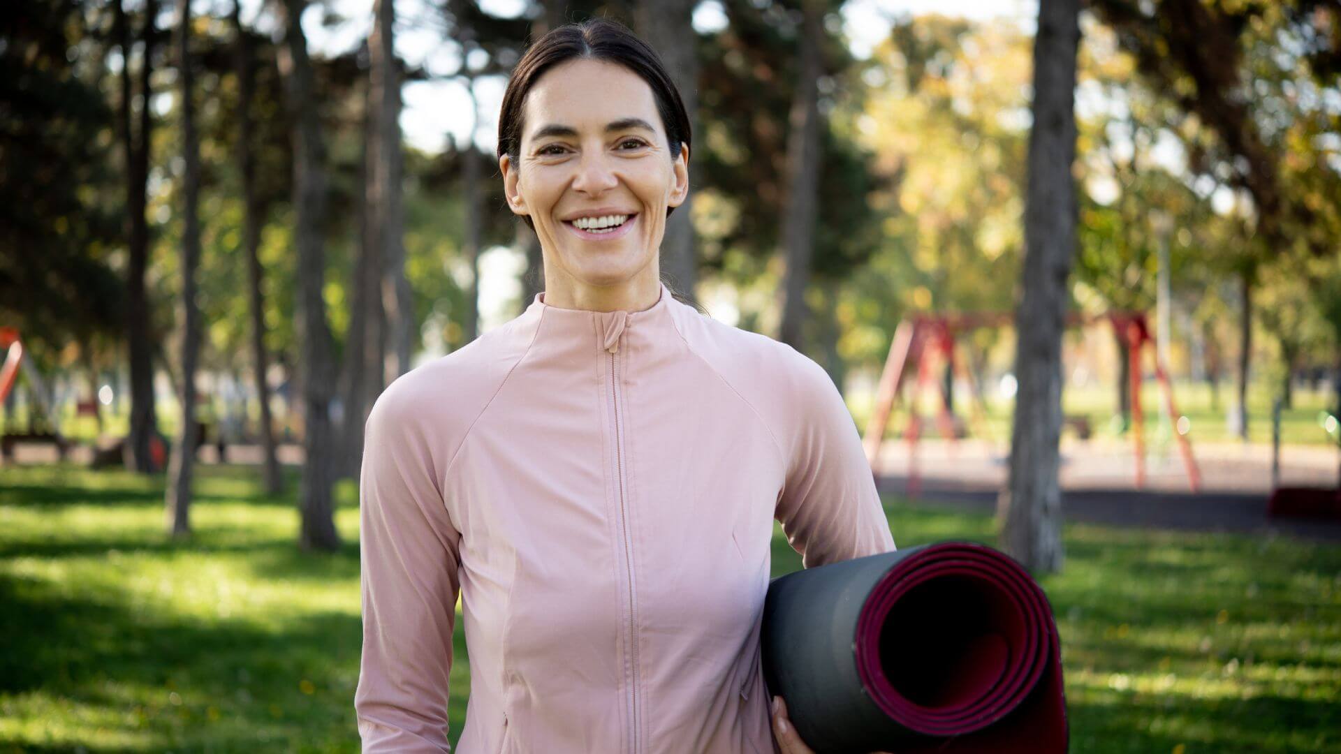 a woman holding a yoga mat in a park