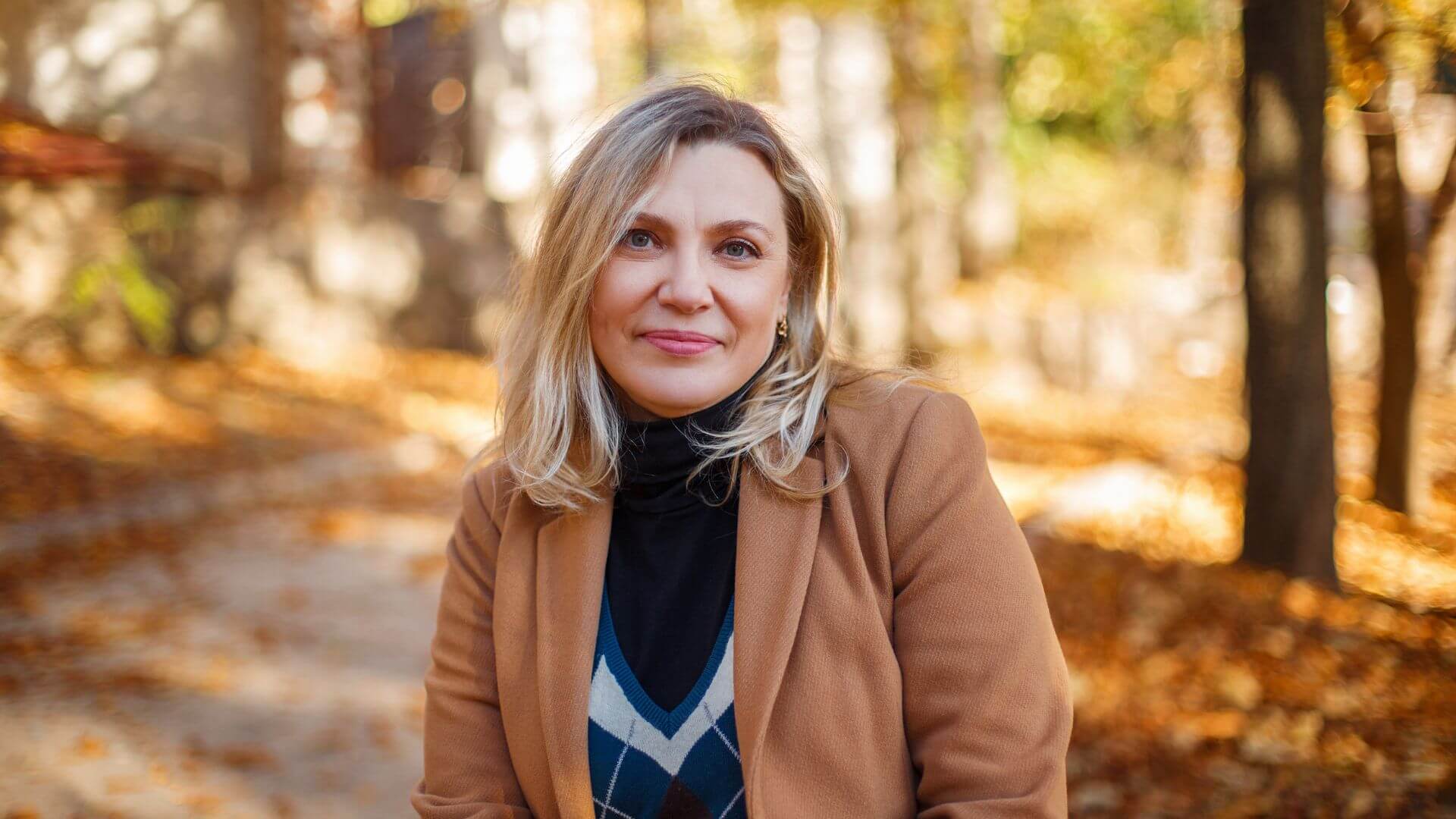 a woman in a tan jacket is sitting in a park