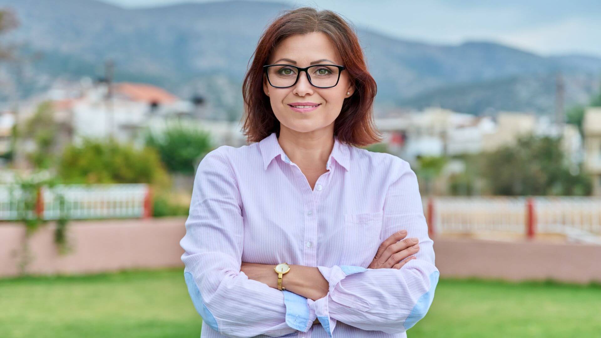 a woman in glasses is standing in a field with mountains in the background