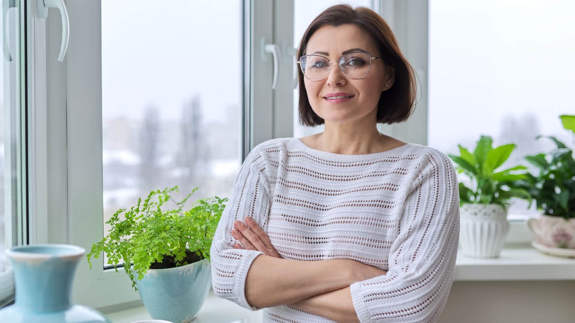 a woman standing in front of a window with plants