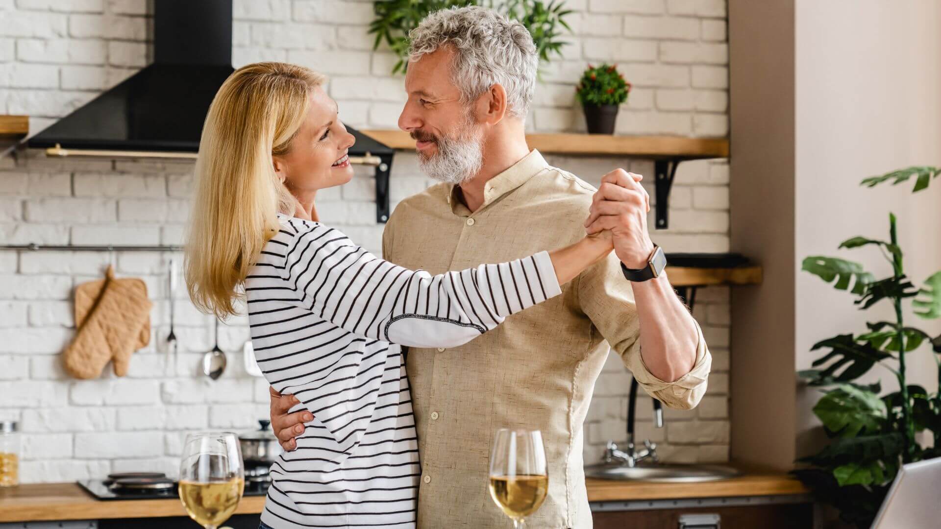 senior couple dancing in the kitchen with wine glasses